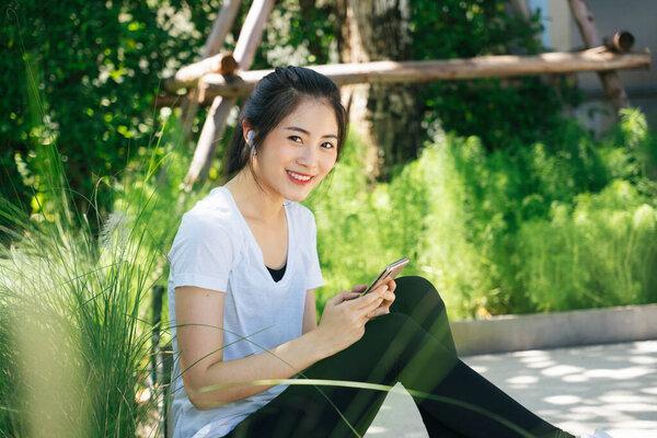 Healthy asian woman take a break using smartphone in park.