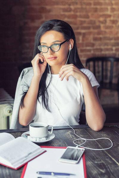 beautiful woman in glasses is listening music by her smartphone at cafe, she listens to music through headphones, portable