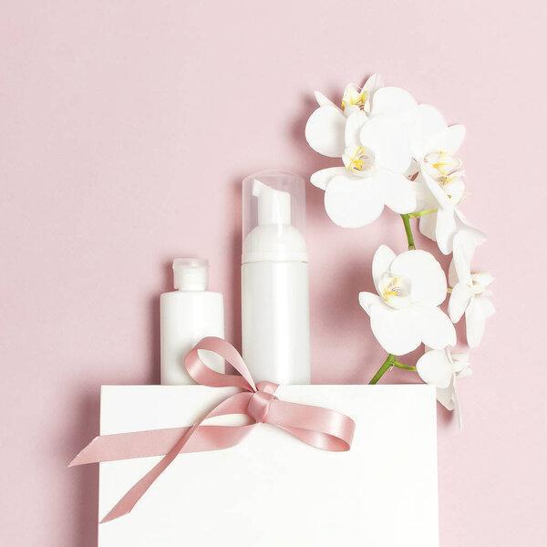Cosmetics SPA branding mock-up. Flat lay top view White cosmetic bottle containers gift bag White Phalaenopsis orchid flowers on pink background. Natural organic beauty product concept