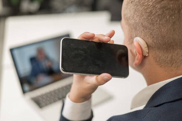 Caucasian man with a hearing aid talking on the phone on speakerphone