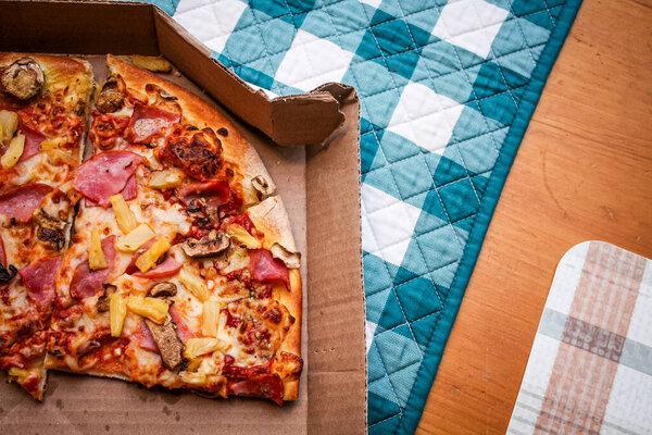 Three slices of pizza that were eaten were left in a cardboard box. Placed on a maple-colored wooden table. And a green plaid placemat.