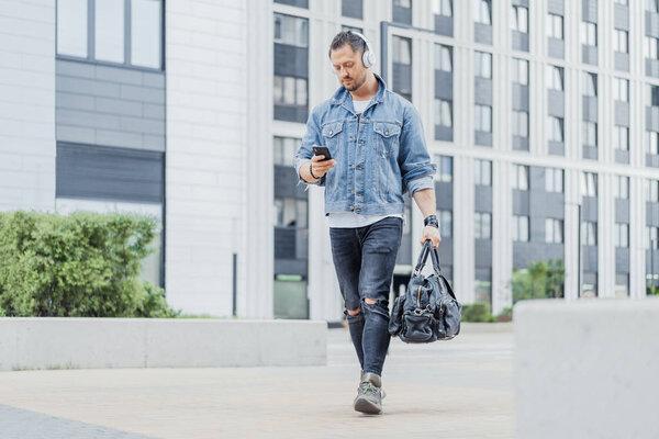 Distant plan of man in earphones looking at his mobile phone while going.