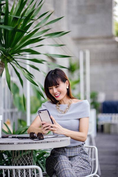 Portrait of an attractive, confident and successful Chinese Asian woman. She is holding her smartphone 