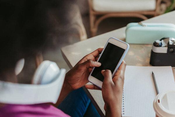 Close up of stylish African woman with headphones looking at screen of mobile phone