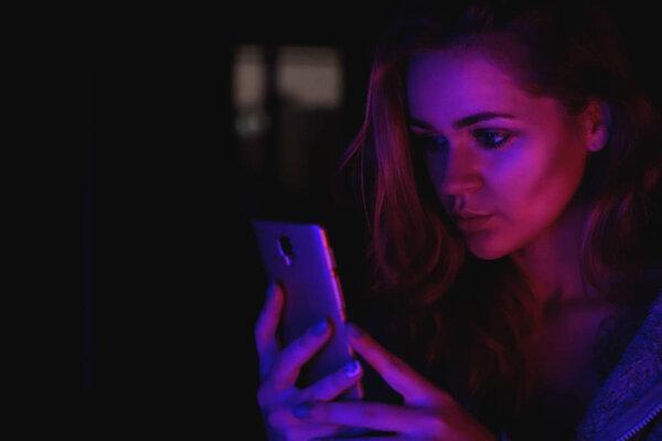 Girl using cellphone at night with neon light - pink and blue