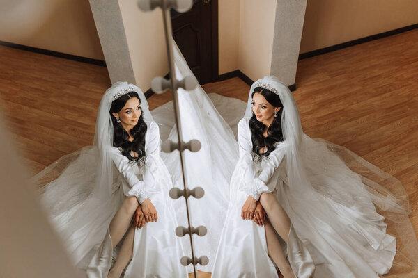 婚礼前的早上，一位漂亮的新娘穿着礼服坐在一间有现代室内装潢的宾馆里。令人难以置信的新娘发型。自然和现代的化妆.