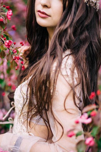 portrait of beautiful young brunette woman in beige Bridal boudoir lace dress, long hair, next to the Sakura tree with pink flowers