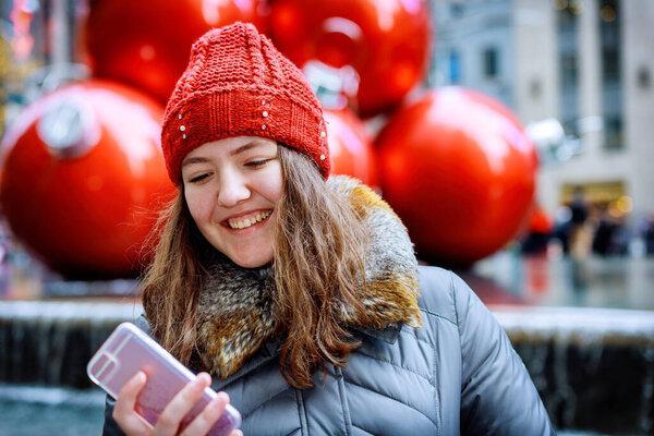 Girl walking and texting on smartphone in the street wearing a red hat