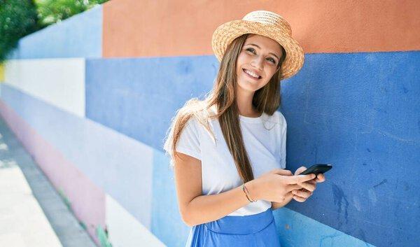 Young blonde woman on vacation smiling happy using smartphone leaning on the wall at street of city