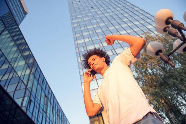 happy smiling urban hipster young man using smart phone. African american teenager holding mobile smartphone on sunset with lens flare