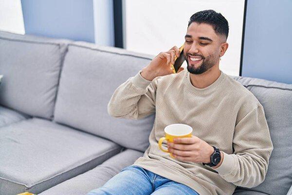 Young arab man drinking coffee and talking on the smartphone at home