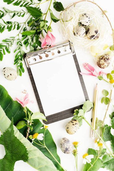 Easter mockup: Top view flat lay notepad and pencil with camomile flowers, leaves and quail eggs in paper nest. Text space