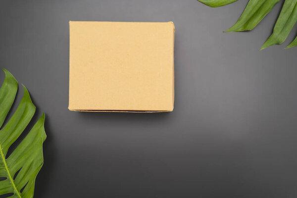 Craft gift box and floral composition with green leaves on black background. Flat lay, top view.