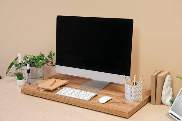 Modern workplace with computer and houseplants near beige wall