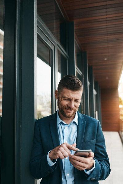 Whenever he steps out, his connections follow. a mature businessman using his cellphone on the office balcony