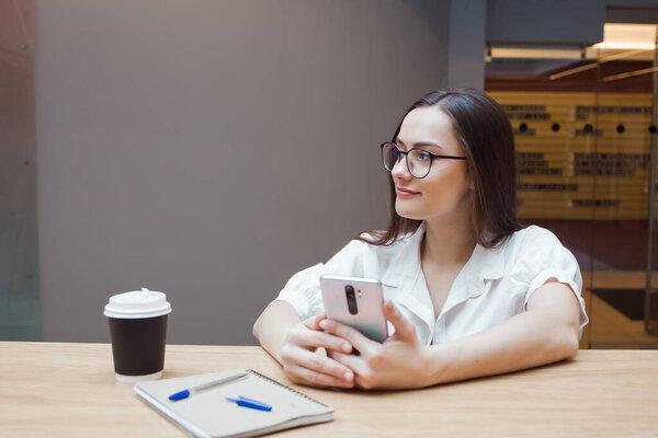 student girl is sitting at a table and using an app on her smartphone.