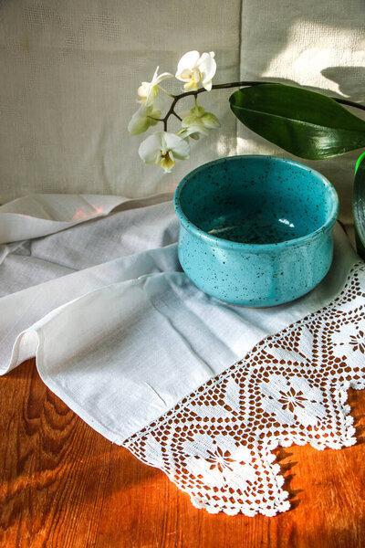 mocap old wooden board and blue plate on white linen tablecloth and lace towel, white orchid flower, sunlight natural light, shade. kitchen table. Nice retro, rustic background, free space.