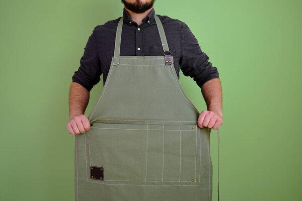 A man in a kitchen apron. Chef work in the cuisine. Cook in uniform, protection apparel. Job in food service. Professional culinary. Green fabric apron, casual stylish clothing. Handsome baker posing