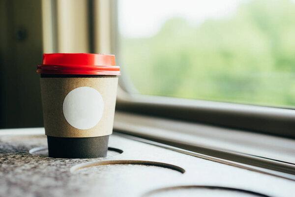 A paper coffee cup with a red plastic lid and a white inscription circle