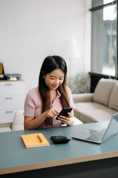 Female student learning at the desk using smartphone to search online information