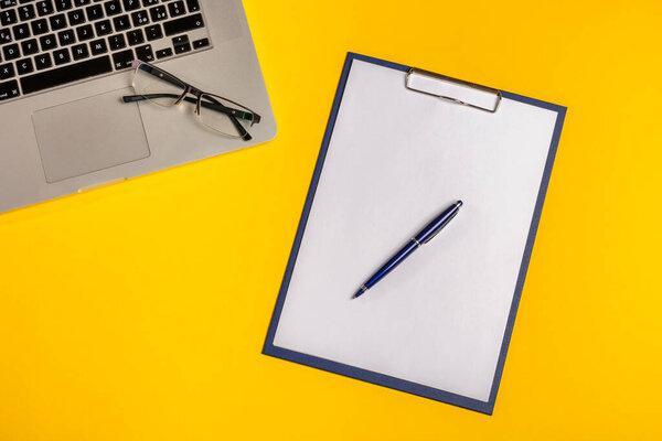 Flat lay out. Computer on yellow background with paper folio, pen and glasses. Business concept idea. Copy space.