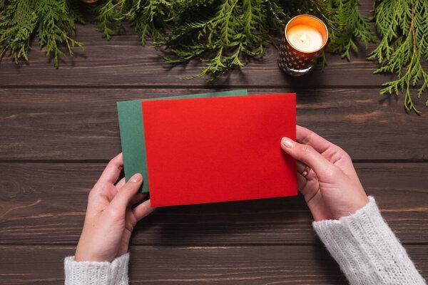 Womans hands holding blank red and green envelopes on wooden background. Chritsmas design.
