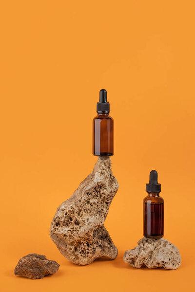 Serum or essential oil in brown glass dropper bottle on stones, orange background. Natural Organic Spa Cosmetic concept Front view.