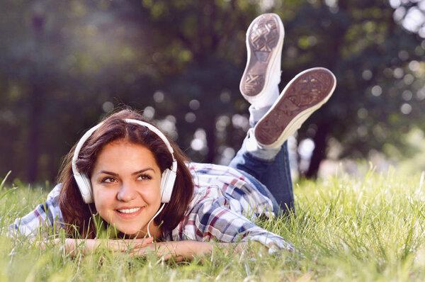 Close up portrait of Pretty young girl listening music lying at the grass