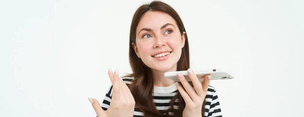 快乐的年轻女子的画像，学生记录语音讯息，把智能手机放在嘴边，对着手机说话，解释某事，唱歌，翻译她的话.
