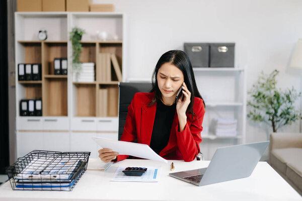 Asian Business woman using smartphone and laptop with a smile while sitting at office
