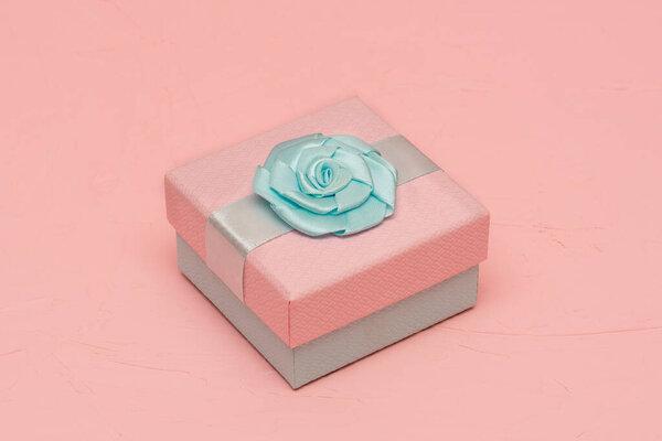 Pink gift box with blue bow on the lid. Pink textured background. Gift, holiday concept.