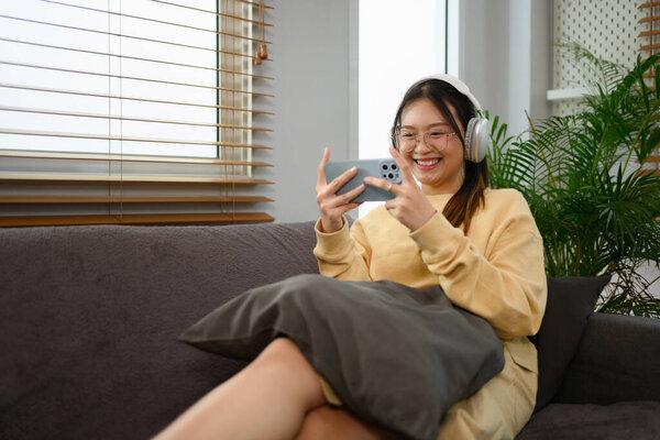 Joyful young woman wearing headphone play video games on smartphone mobile phone at home.