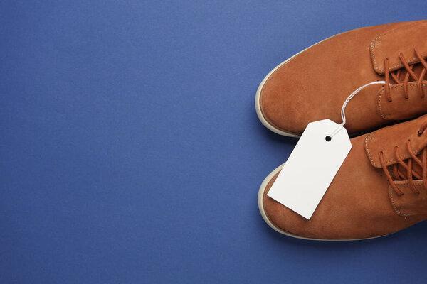 Suede shoes with white blank tag on string, blue background. Template for design, sale, shopping concept