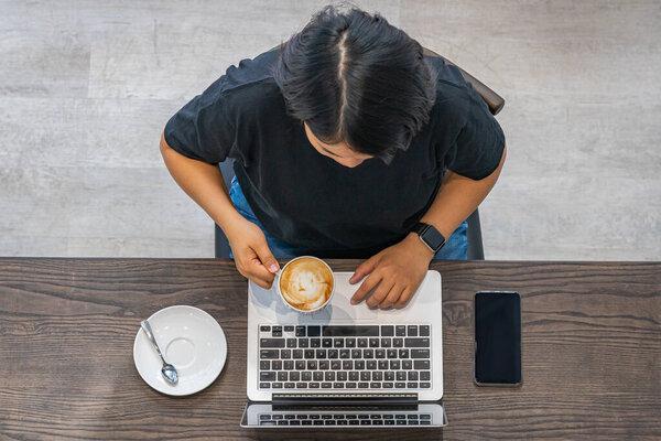 Asian woman having hot latte and working on laptop