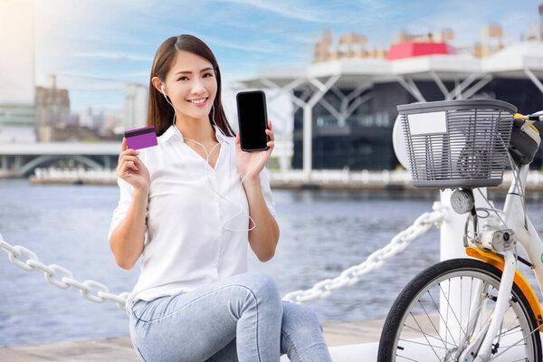 Young woman showing mobile phone and credit card for Bike sharing service.