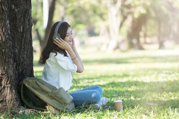 Young Asian casual hipster girl listening to music in city park