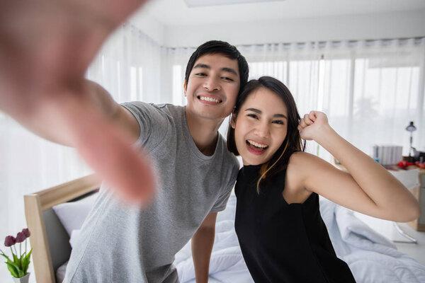 Asian couple lovers lying on their play mobile phones and selfie on bed  at home