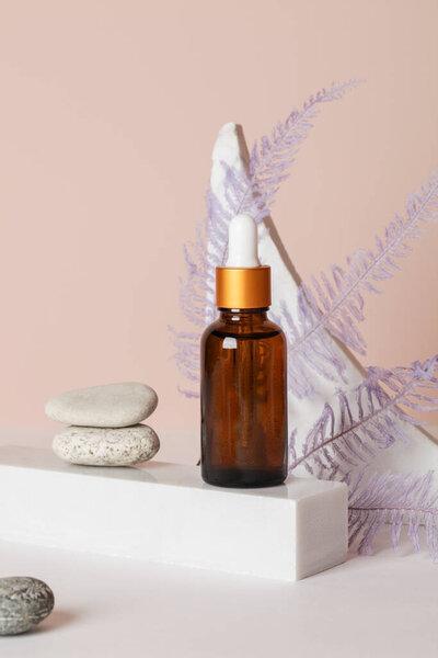 dark amber glass bottle with oil on pedestal with fern on beige background. copy space. natural cosmetics and body care concept , mock up