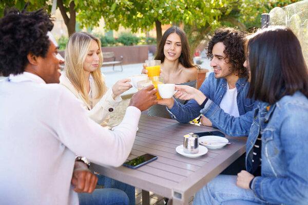 Multi-ethnic group of friends toasting with their drinks while having a drink together.