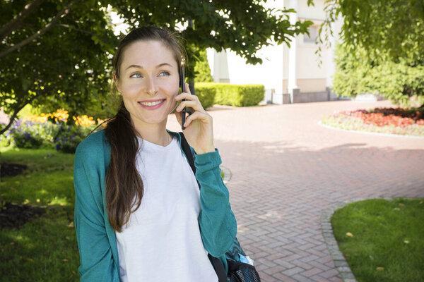 An outdoor portrait of young woman talking on the phone in a city park on a sunny day.