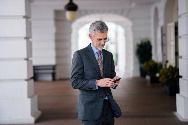 portrait of Senior businessman wearing suit with smartphone on city background