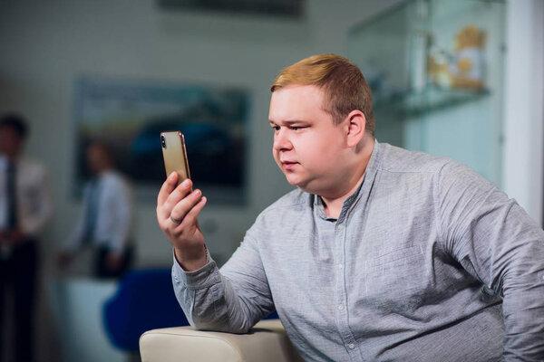technology, people, lifestyle and communication concept - happy man with smartphone having video call home and showing thumbs up sitting on sofa in office
