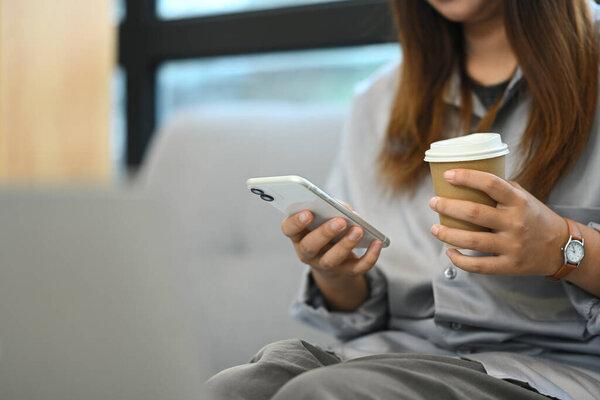 松懈的年轻女工躺在办公室沙发上喝咖啡，用手机.