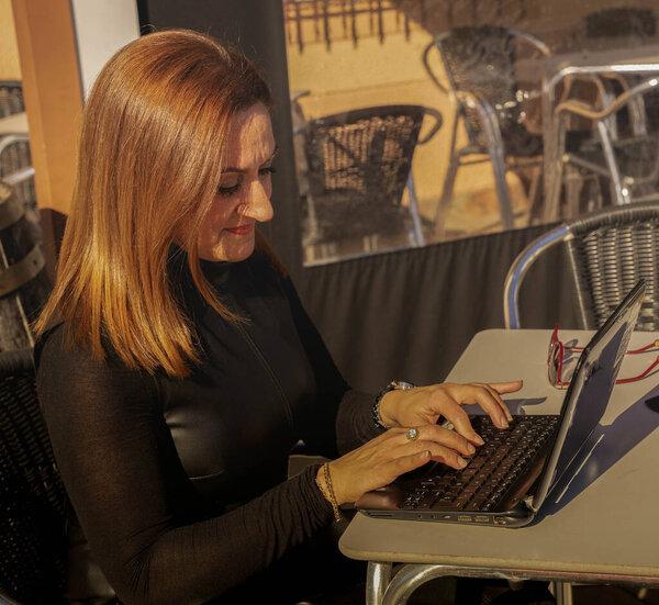 middle-aged woman sitting at a table with a laptop looks into the camera