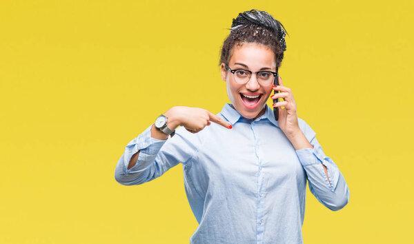 Young braided hair african american business girl showing calling using smartphone over isolated background with surprise face pointing finger to himself