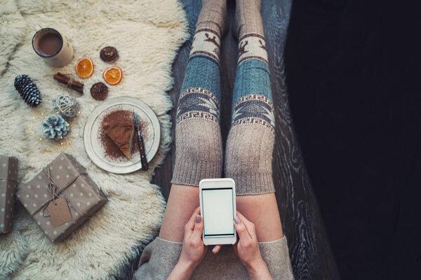 Woman using smartphone for browsing internet store at home. Online shopping conceptspace for text. Mood winter. Seasonal holidays. Merry Christmas and New Year. Top view. Toned image. Selective focus.