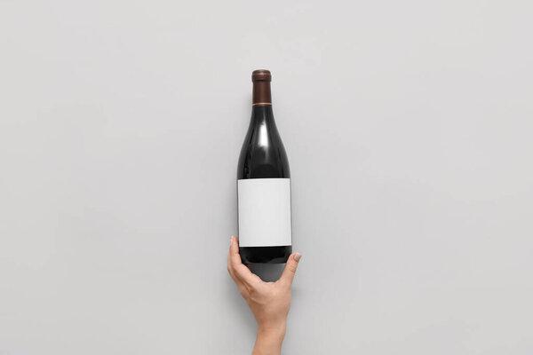 Female hand and bottle of wine with blank label on light  background