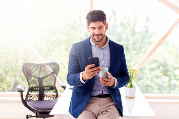 Shot of thinking businessman using his mobile phone and text messaging while sitting at office desk and working.Home office.