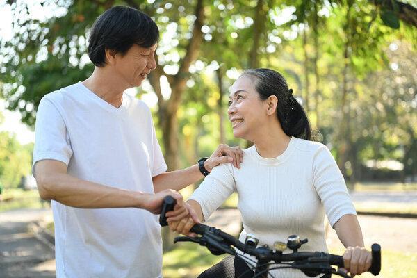 拍快乐退休夫妇骑自行车在夏季公园。健康生活方式概念