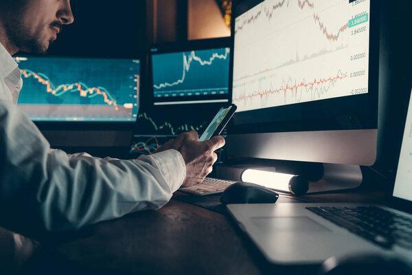 Confident male financial broker using technology and analyzing stock market data while working late in office